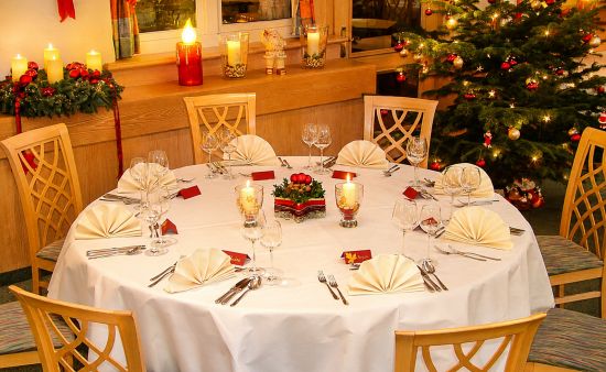 festlich gedeckter runder tisch im wintergarten, mit kerzen und weihnachtsbaum